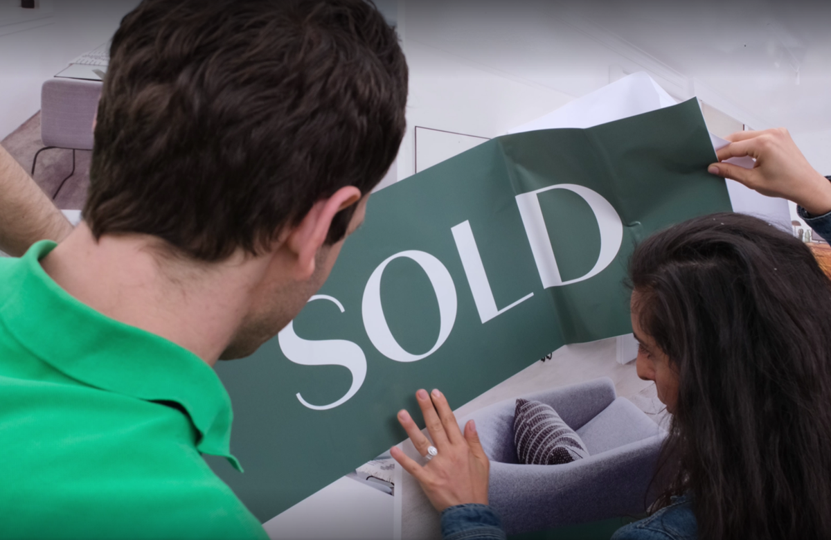 Young couple placing SOLD sticker on property sign board